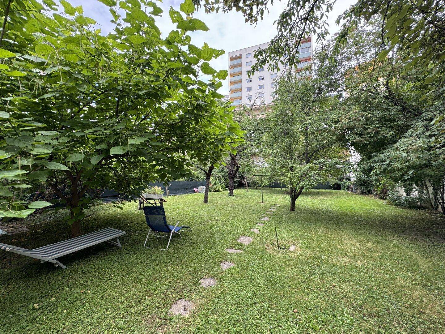 Großer grüner Garten mit Rasenfläche, Bäumen und Liegestühlen.