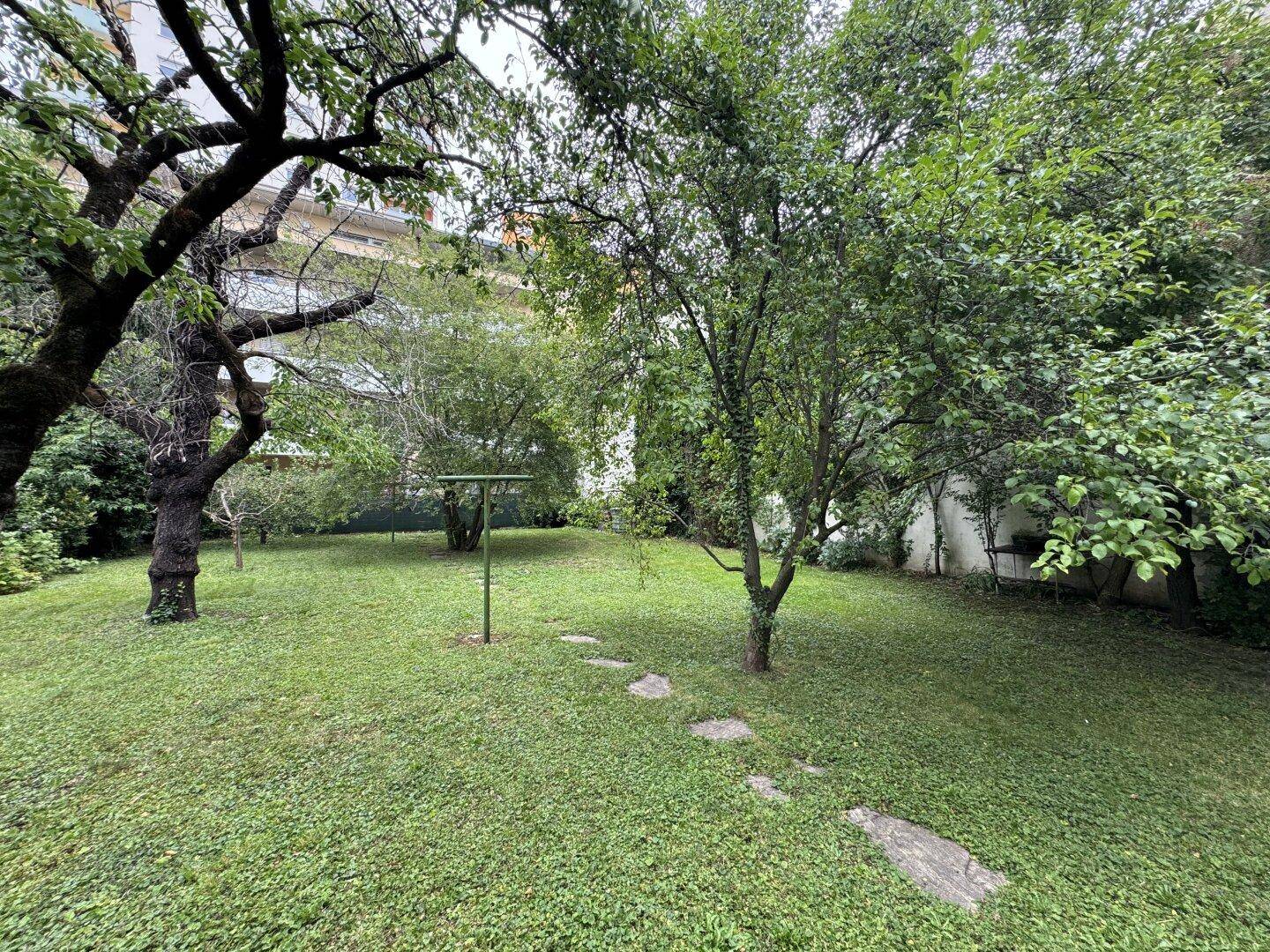 Weitläufiger Garten mit Rasen, alten Bäumen und einem Pfad aus Trittsteinen.