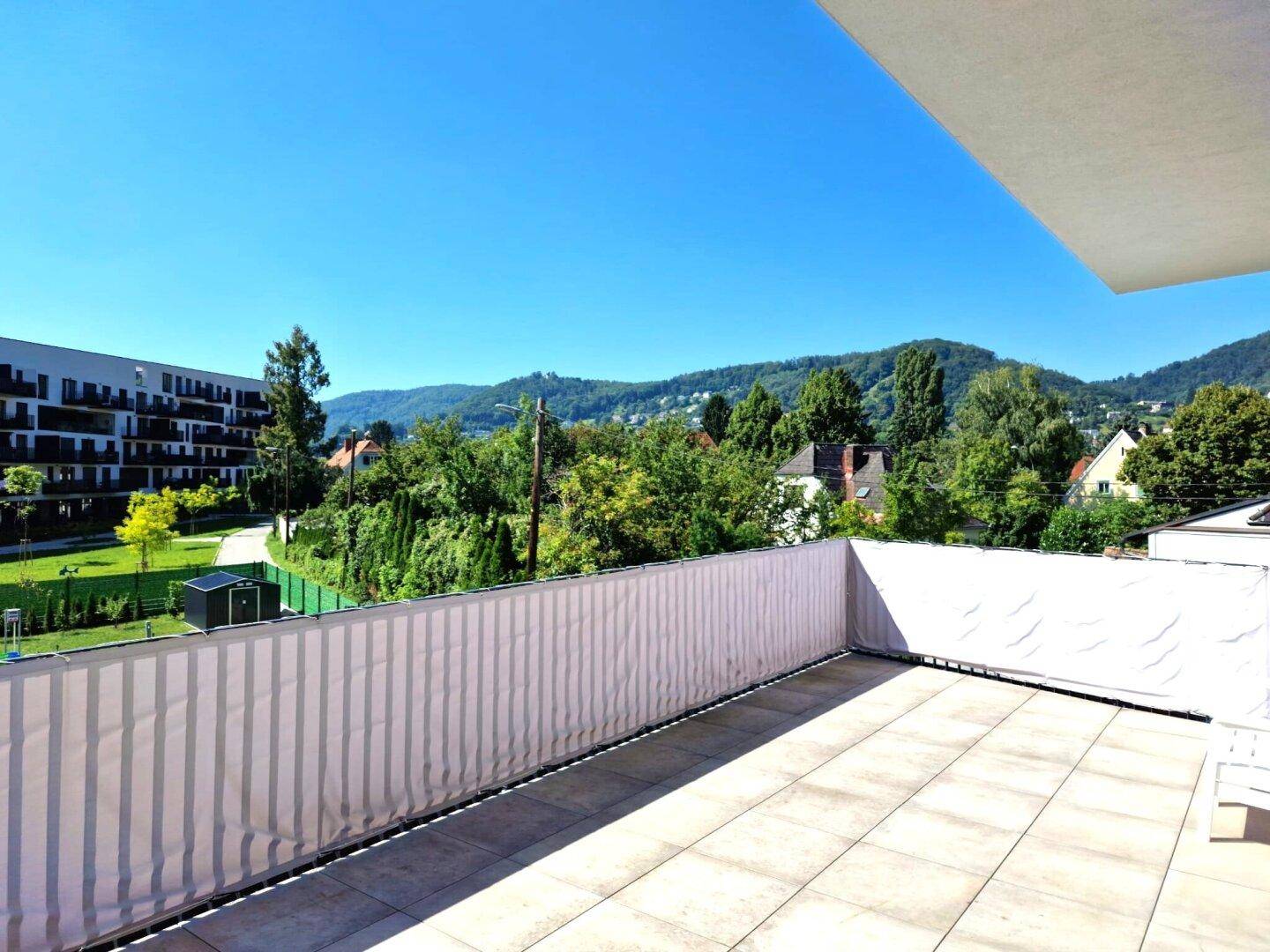 Geräumige Terrasse mit weitem Blick auf die grünen Hügel und umliegende Bebauung.