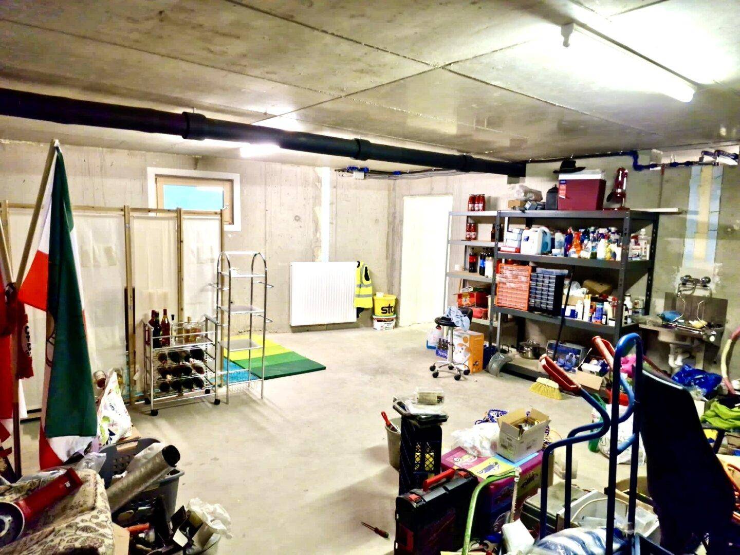 Geräumiger Kellerraum mit Betonwänden, Regalen und sichtbaren Installationen.