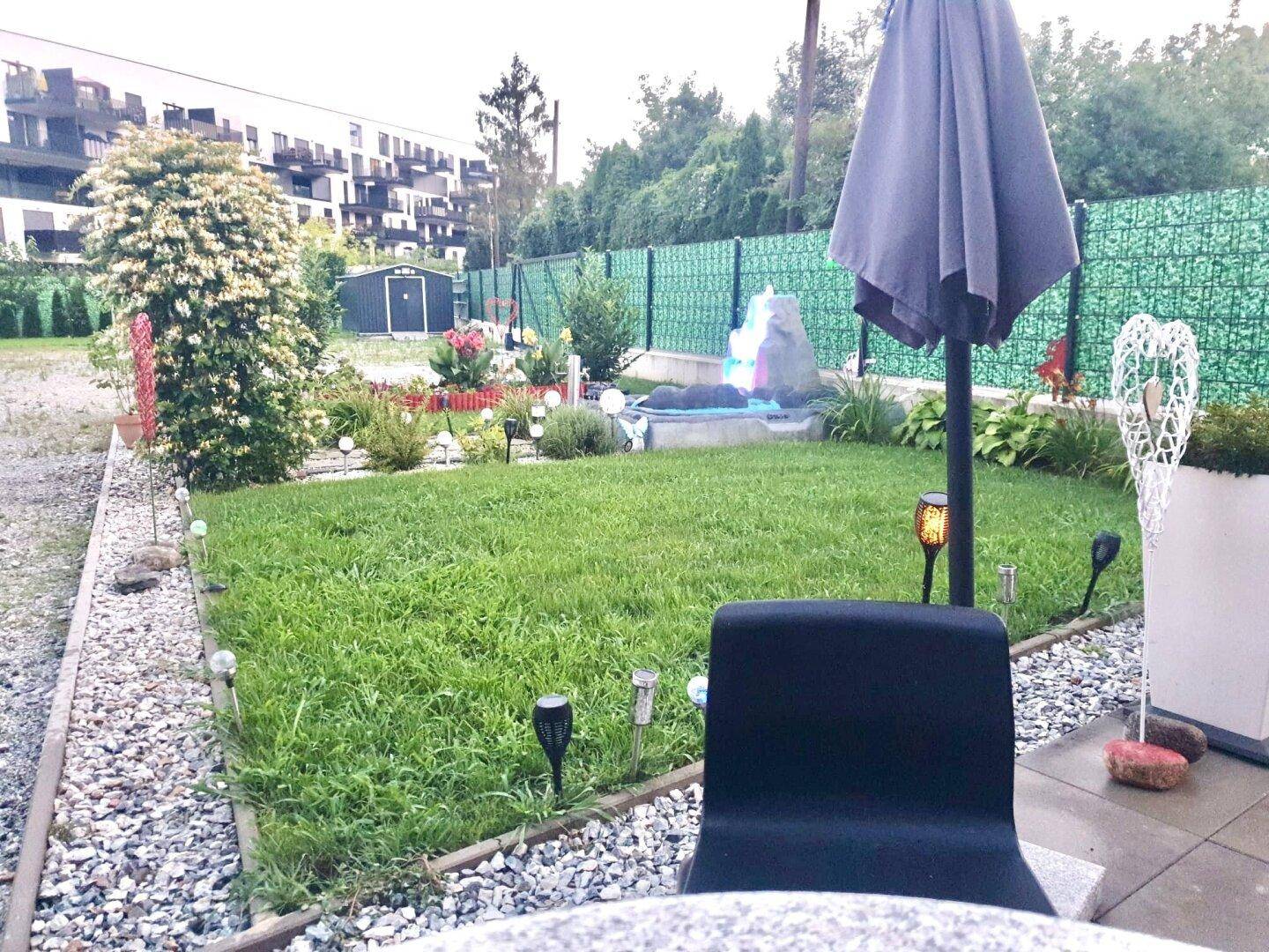 Gepflegter Gartenbereich mit Rasenfläche, Kieswegen und einem Sonnenschirm für entspannte Stunden.
