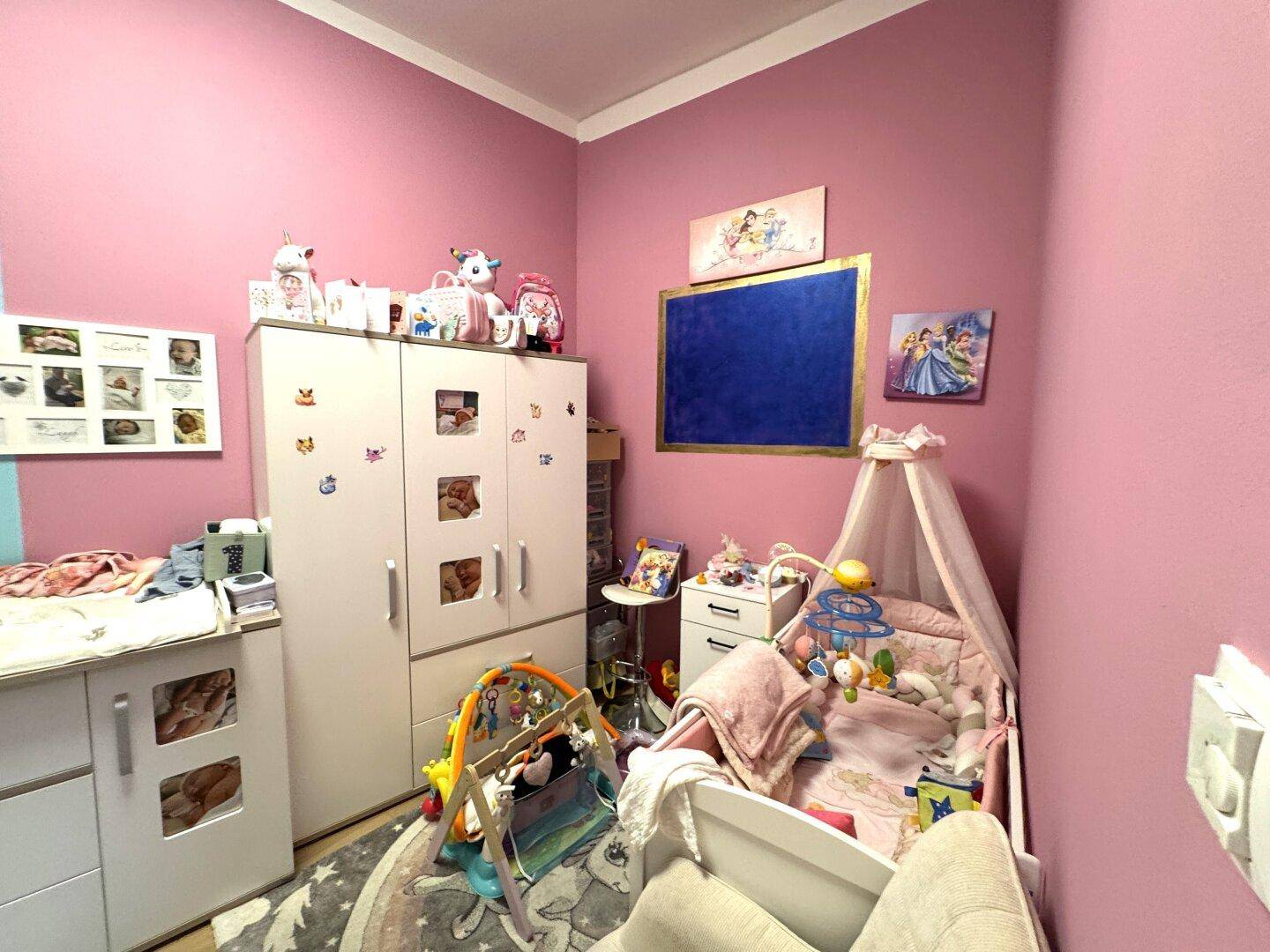 Kinderzimmer mit rosa Wänden, einem Babybett und kindgerechter Dekoration.