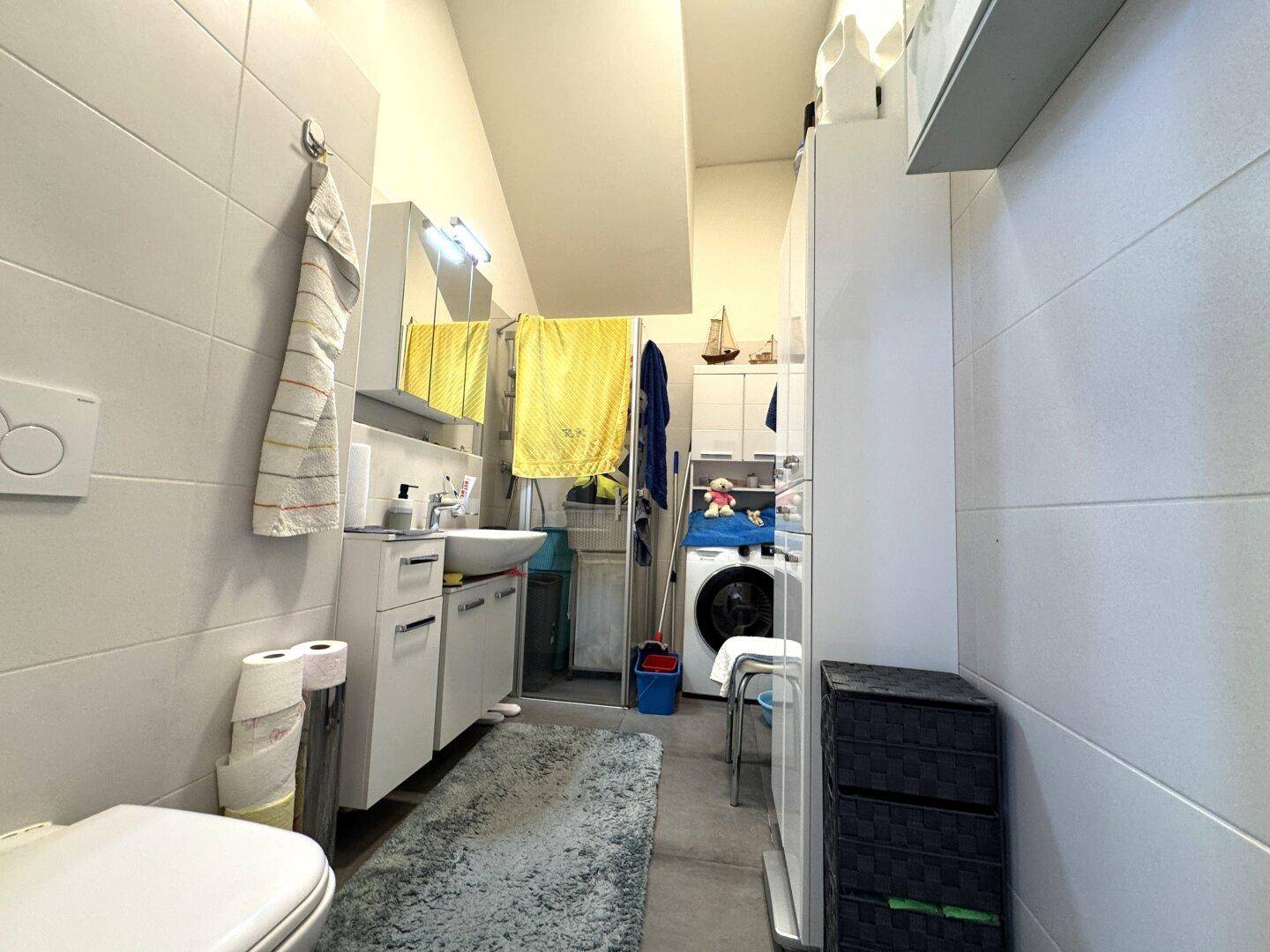 Funktionales Badezimmer mit Toilette, Waschbecken und integrierter Waschmaschine.