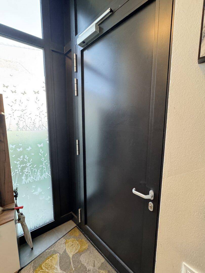 Moderne schwarze Eingangstür mit seitlichem Milchglasfenster, das ein Schmetterlingsmuster zeigt.
