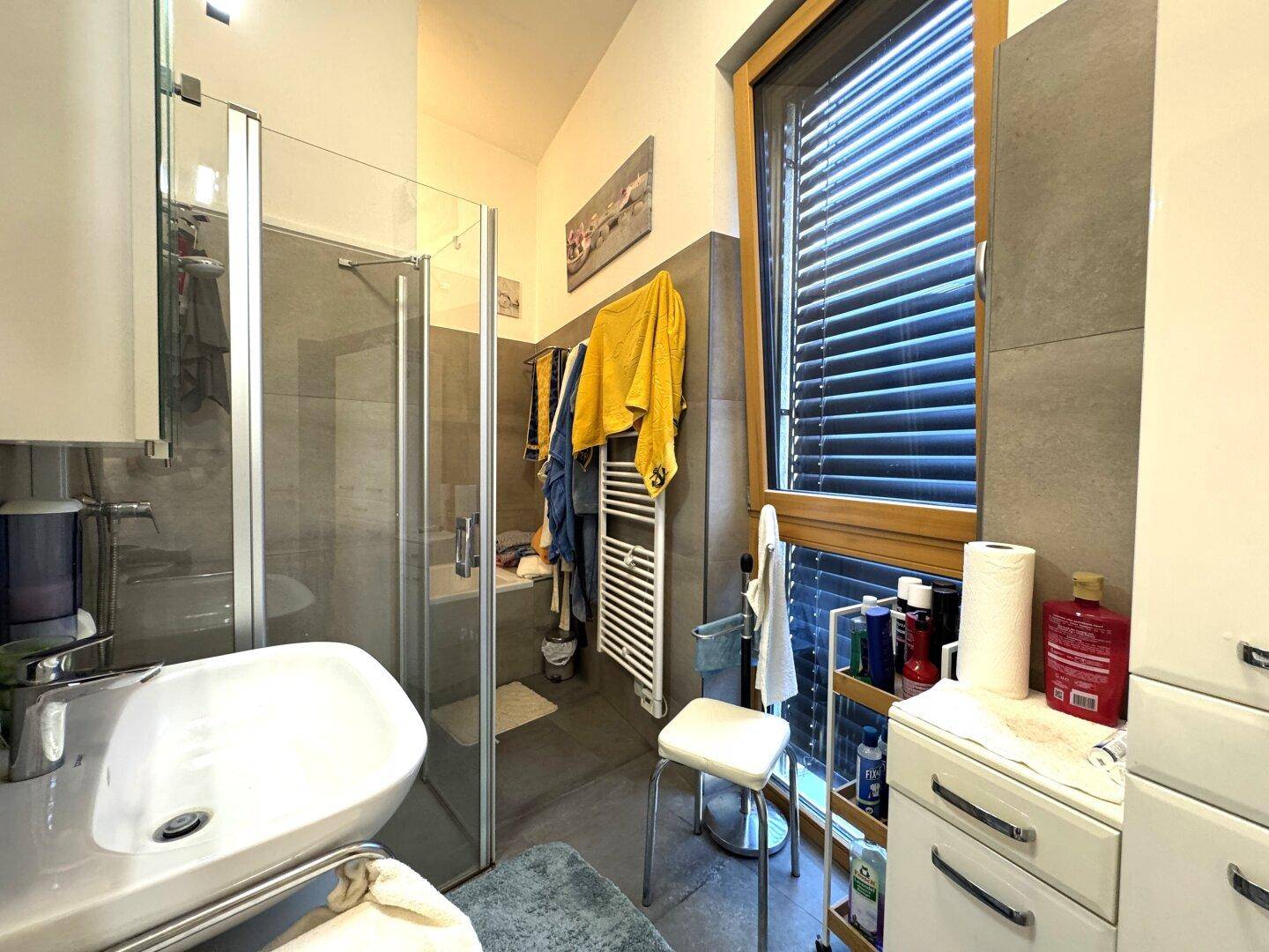 Modernes Badezimmer mit Duschkabine, Waschbecken und einem großen Fenster für Tageslicht.