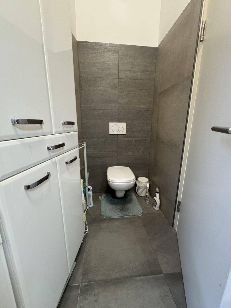 Separates WC mit wandhängender Toilette und praktischen weißen Hochschränken für Stauraum.