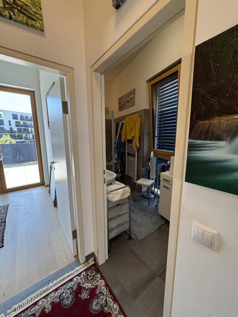 Blick vom Flur in das moderne Badezimmer mit Duschkabine und Fenster.