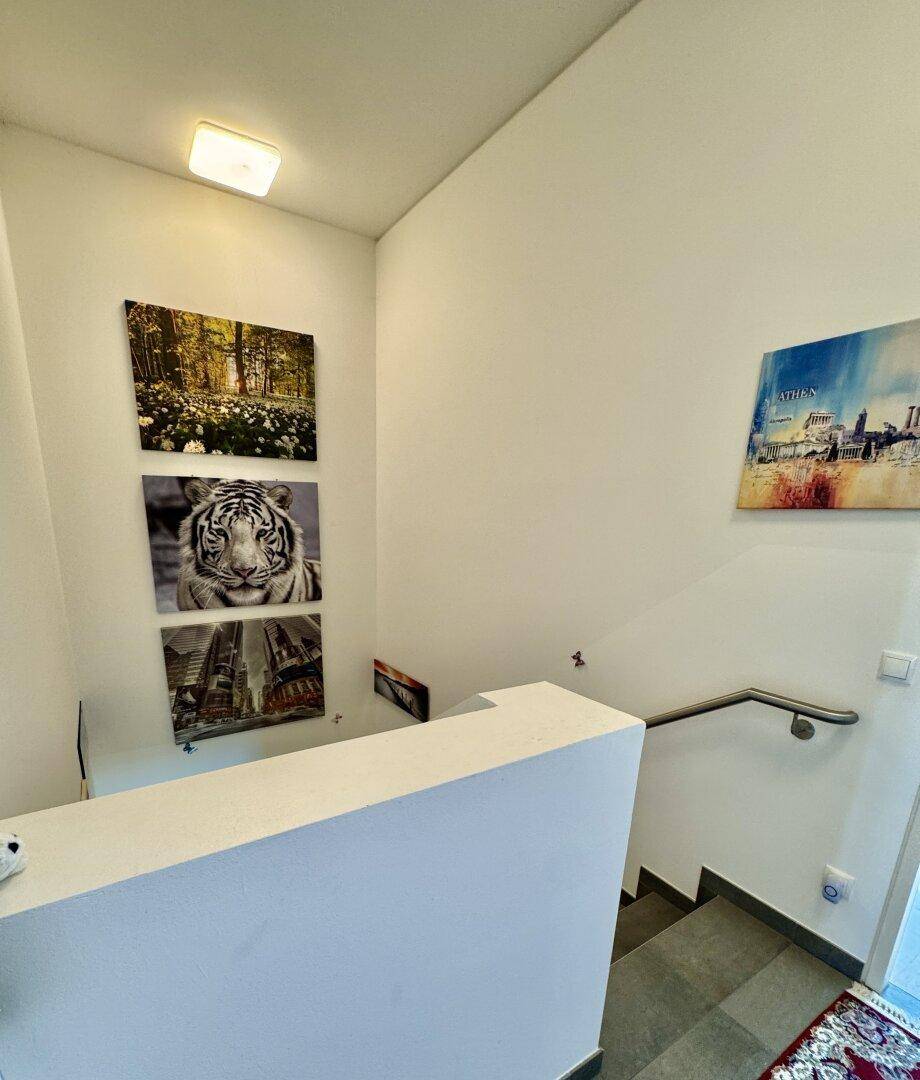 Treppenhaus mit modernen Bildern an der Wand und einem schlichten Handlauf.