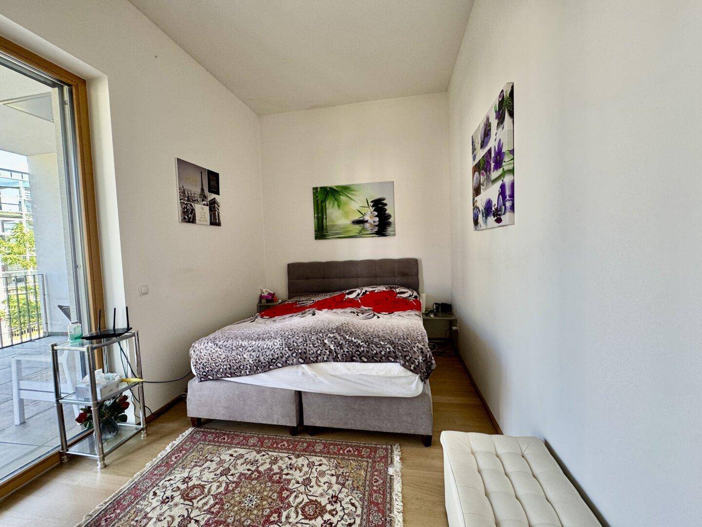 Helles Schlafzimmer mit Doppelbett, Teppich und direktem Zugang zum Balkon.