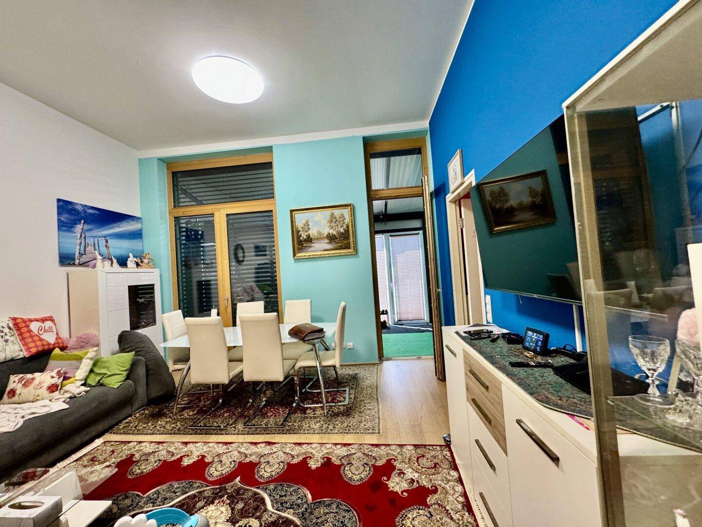 Heller Wohn-Essbereich mit blauer Akzentwand, Esstisch und gemütlichem Sofa.
