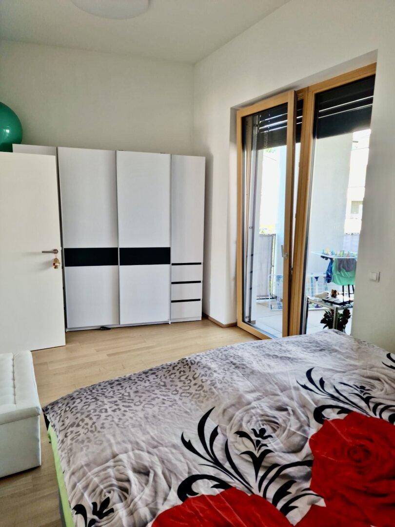 Helles Schlafzimmer mit Holzboden, weißem Kleiderschrank und Zugang zum Balkon.