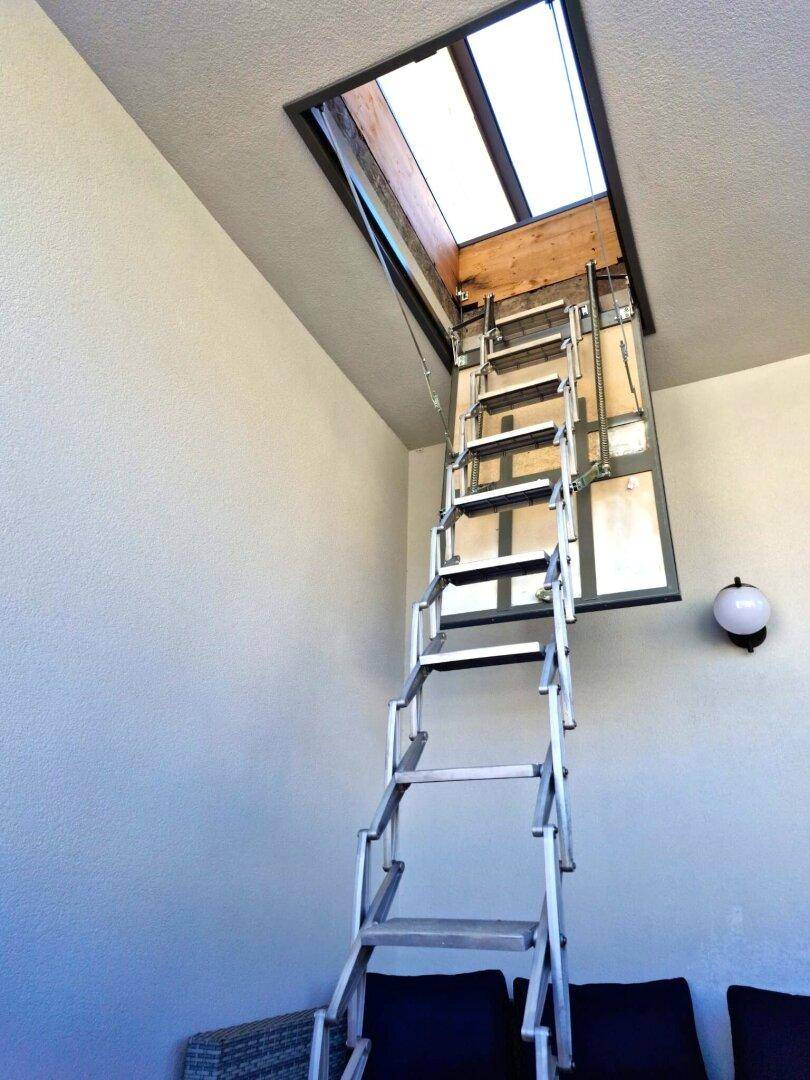 Ausziehbare Leiter zum Dachboden mit einem Dachfenster, das Tageslicht hereinlässt.