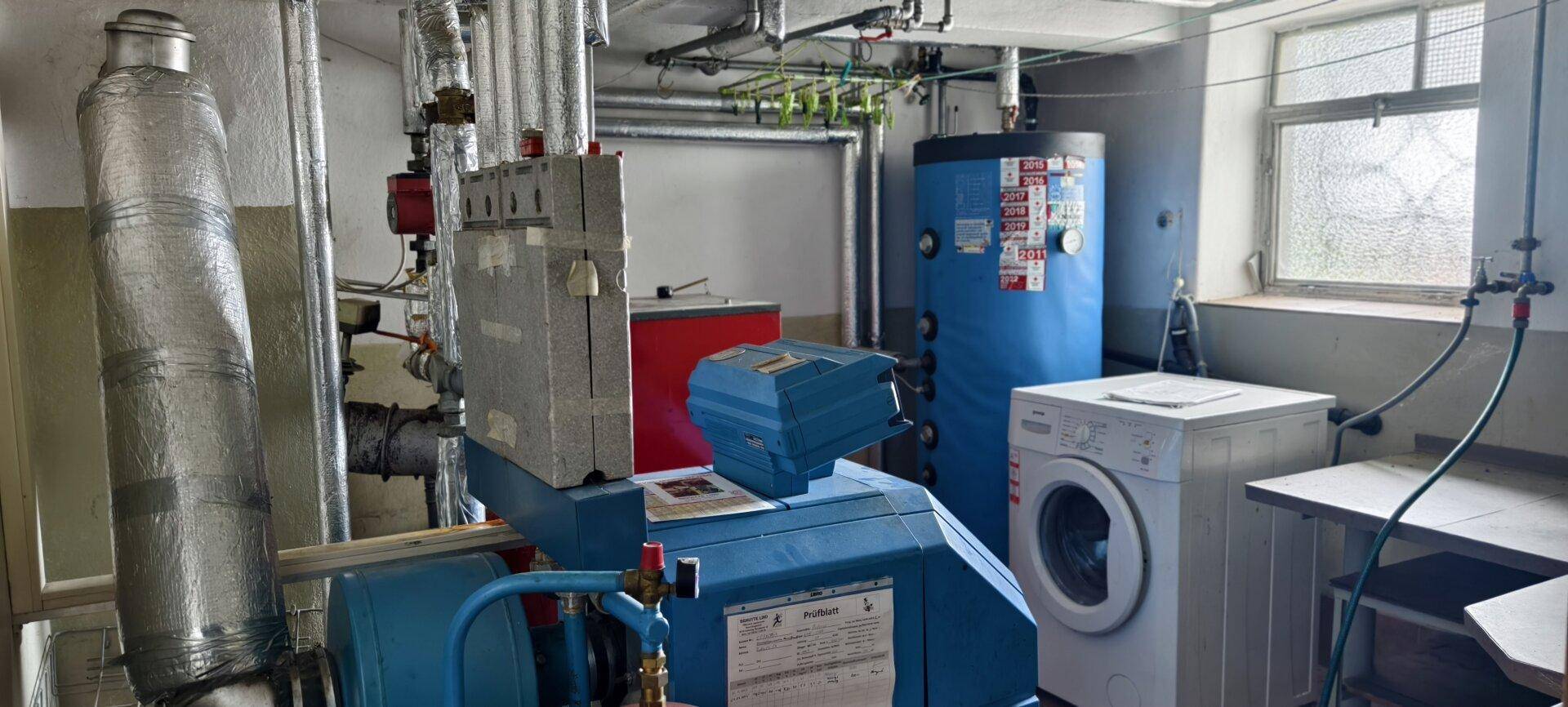 Heizungsraum im Keller mit Waschmaschine, Warmwasserspeicher und umfangreicher Rohrinstallation.