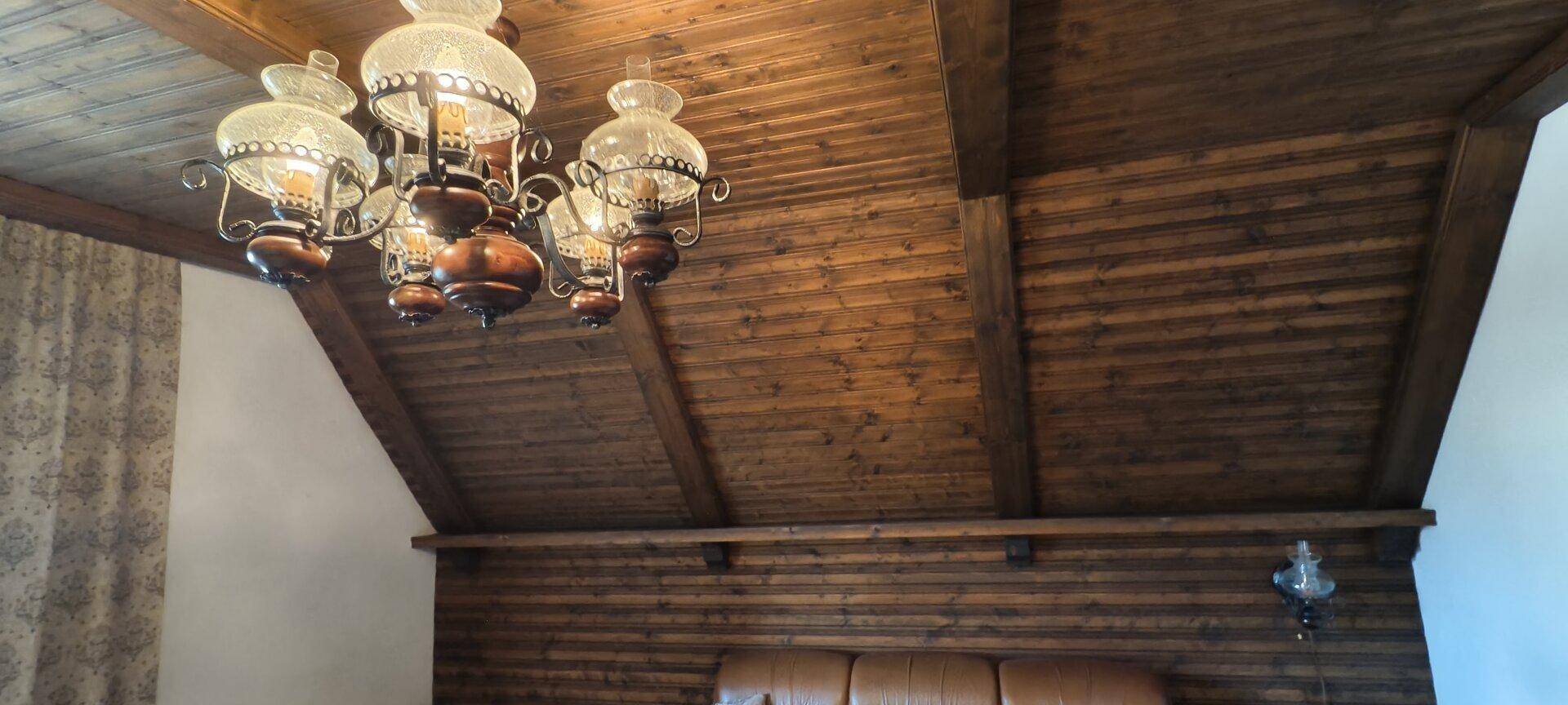 Holzvertäfelte Decke mit sichtbaren Balken und einem klassischen Kronleuchter.