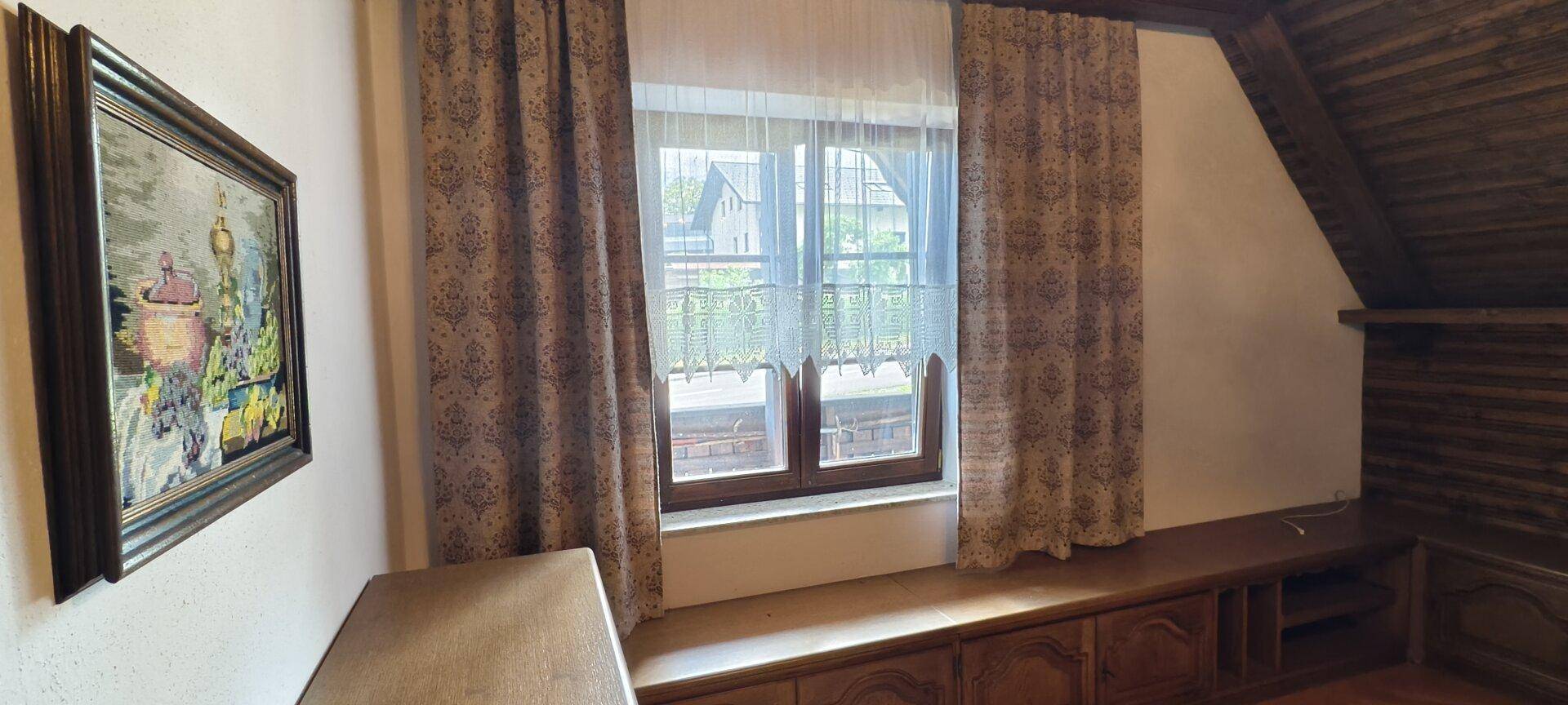 Fenster mit Vorhängen in einem Raum mit Dachschräge und Holzvertäfelung.