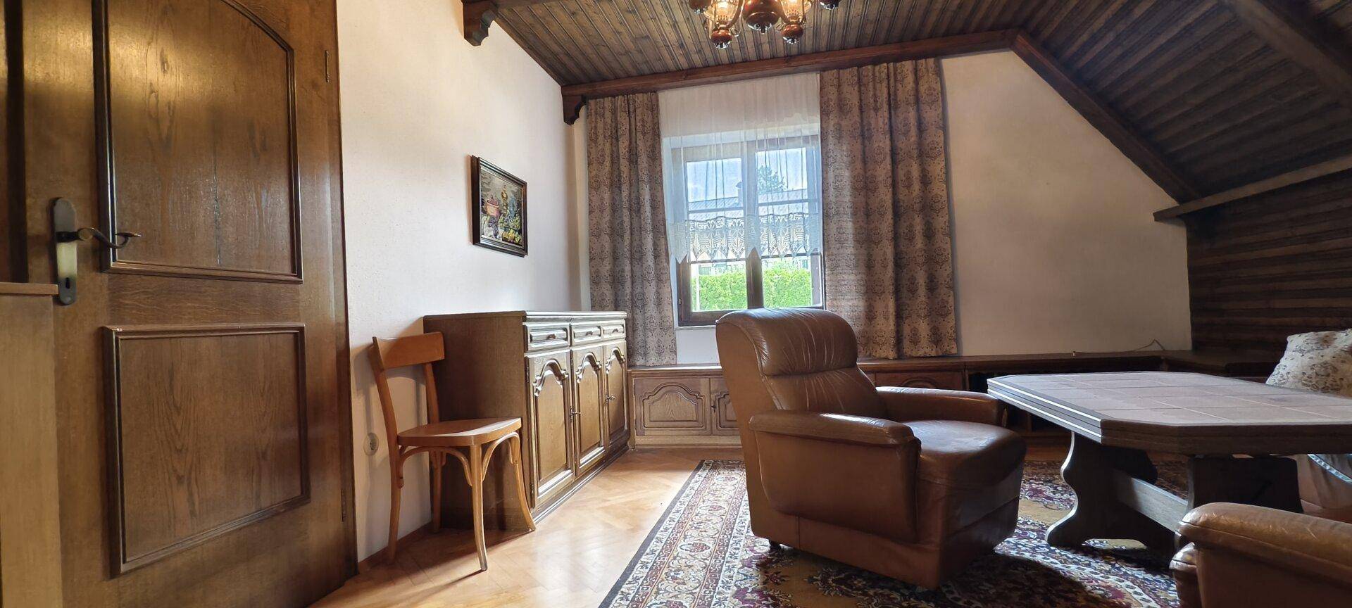 Gemütlicher Wohnbereich mit Dachschräge, Ledersessel und traditionellem Holzschrank.