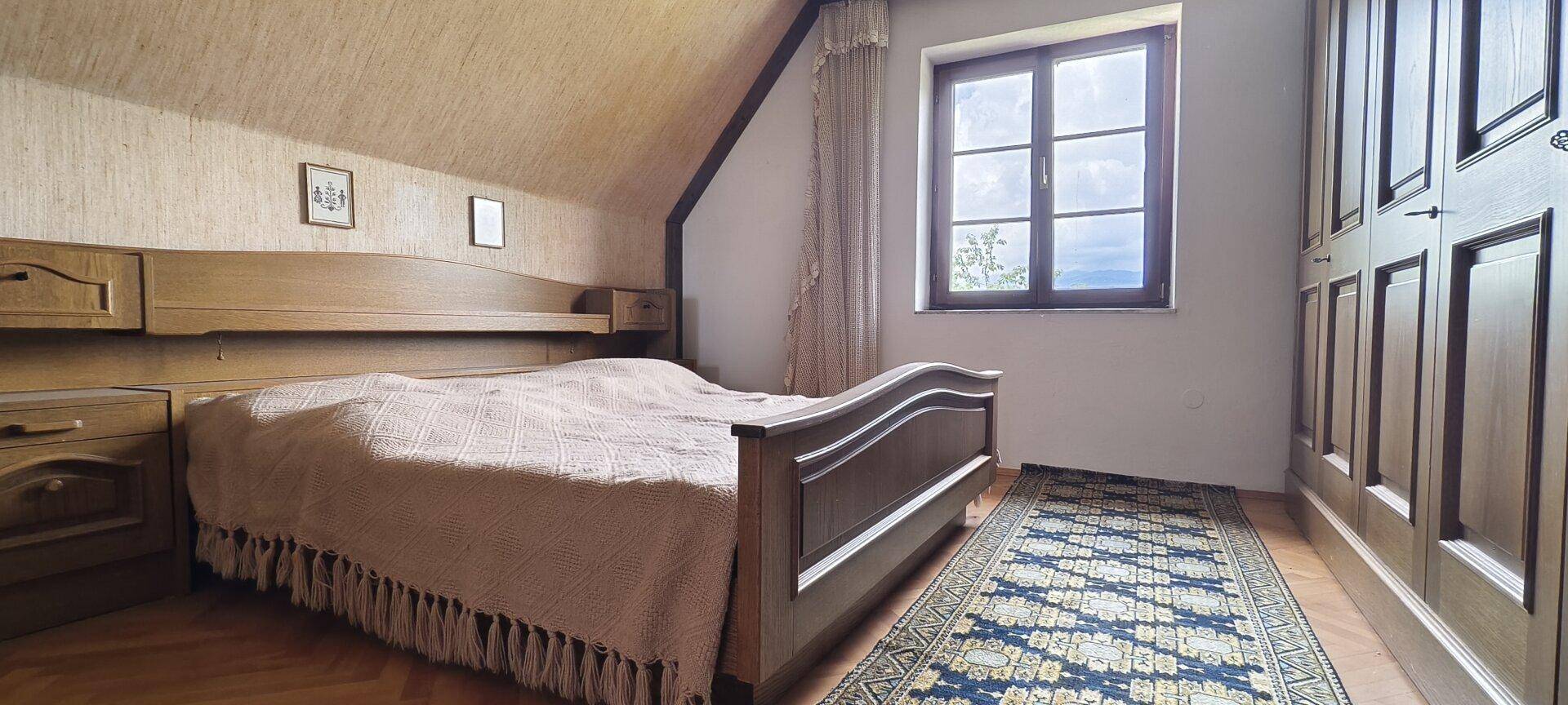 Schlafzimmer mit Doppelbett, Holzmöbeln und Dachschräge.