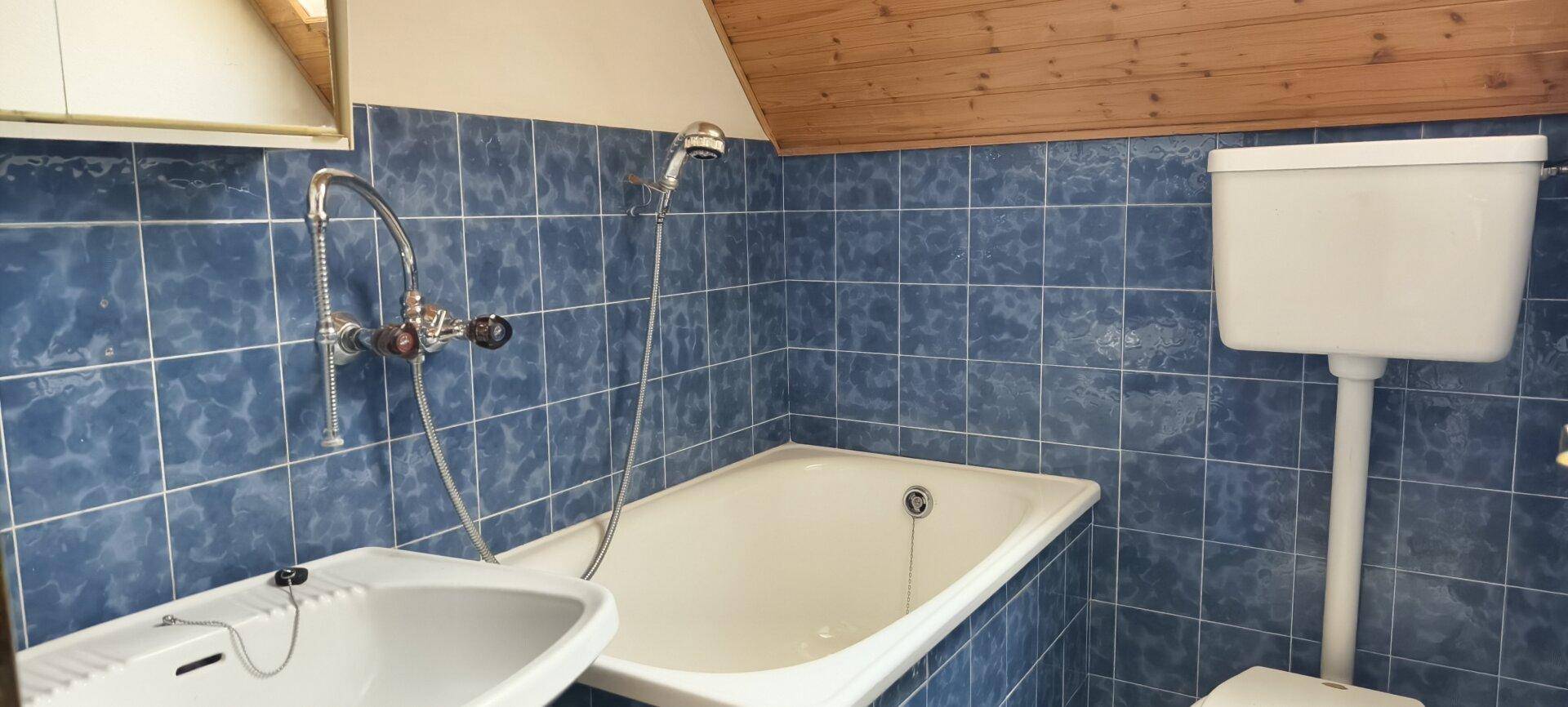 Badezimmer mit blauen Fliesen, Badewanne und Waschbecken unter der Dachschräge.