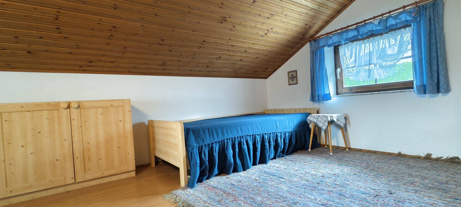 Helles Schlafzimmer mit Einzelbett, Holzschrank und Dachschräge.