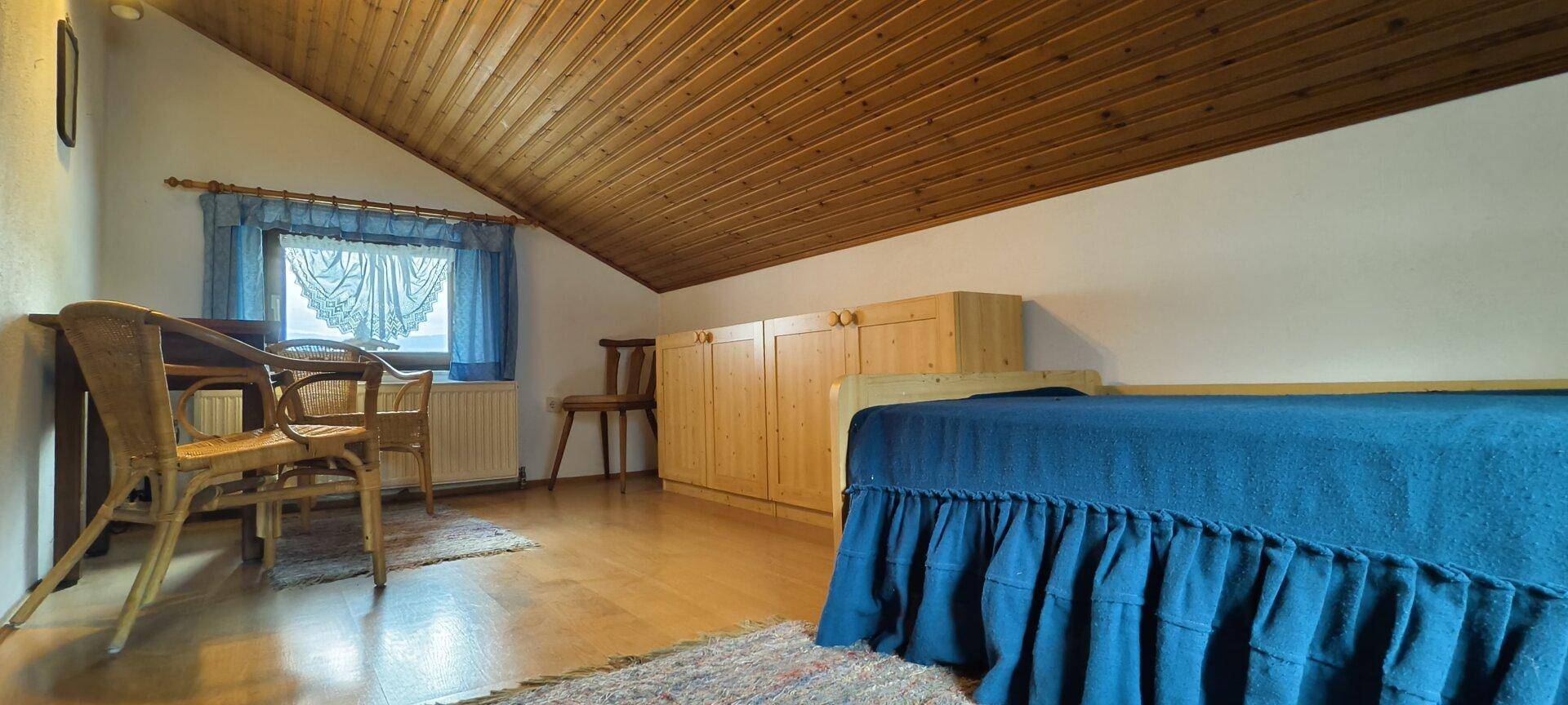 Schlafzimmer mit Einzelbett, Holzdecke und Dachschräge.