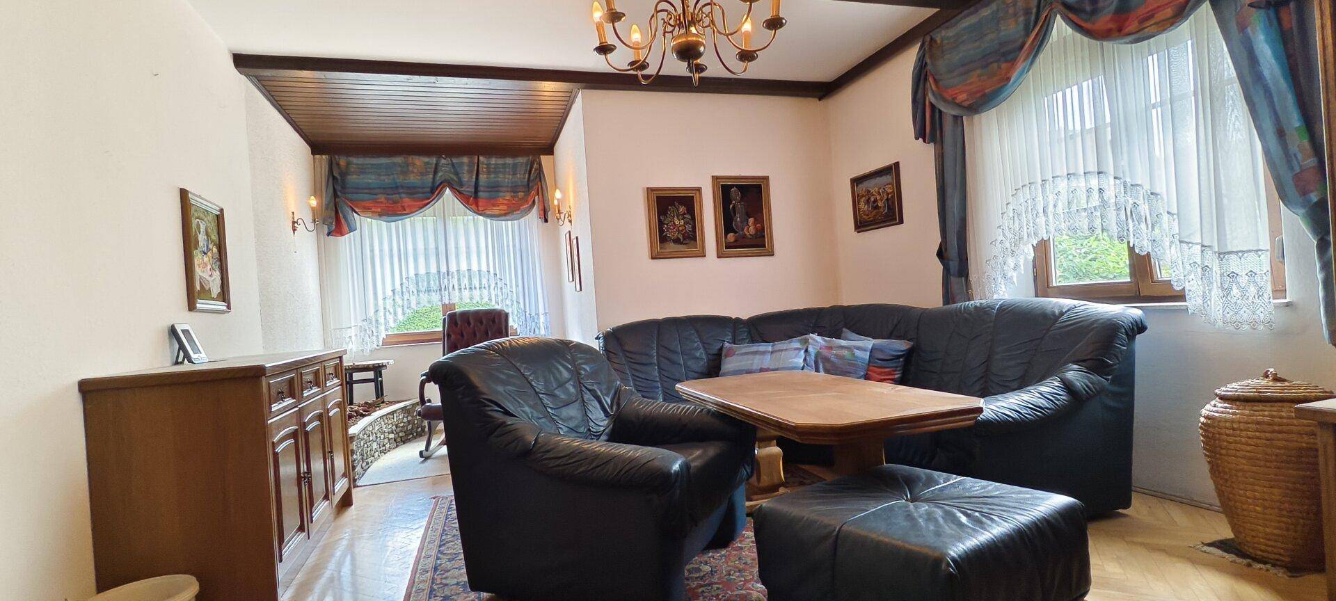Gemütliches Wohnzimmer mit Ledersofas, Holztisch und traditionellen Vorhängen.