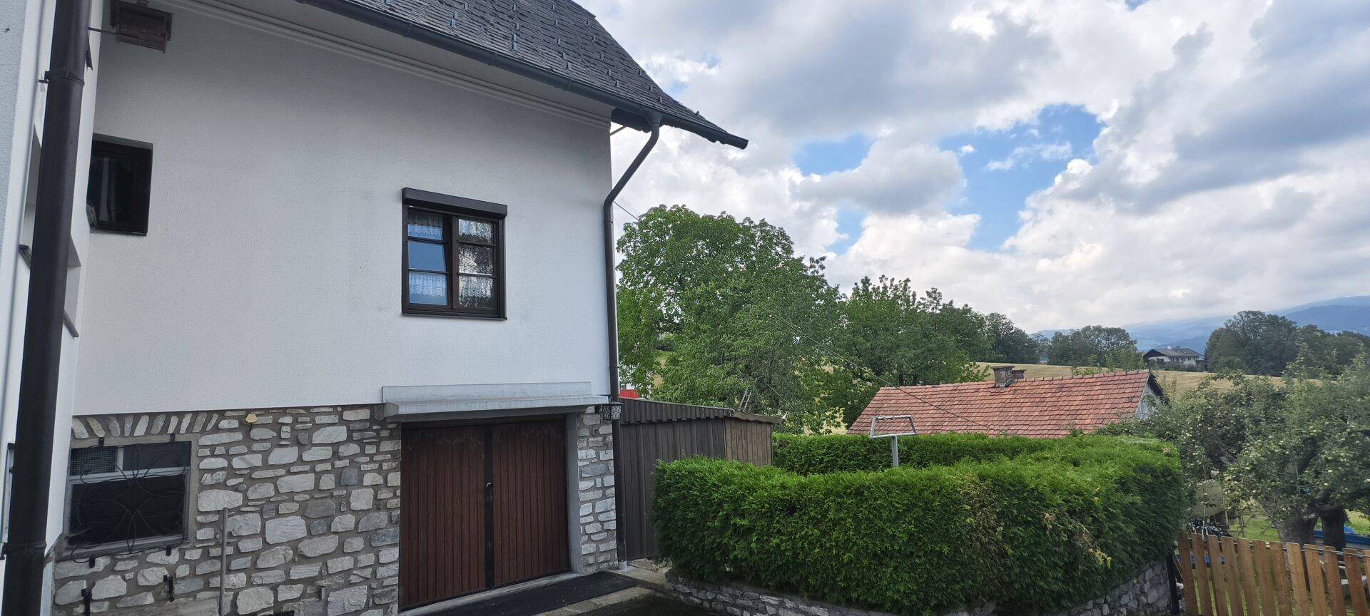Seitenansicht des Hauses mit Steinsockel, Garage und grüner Hecke.