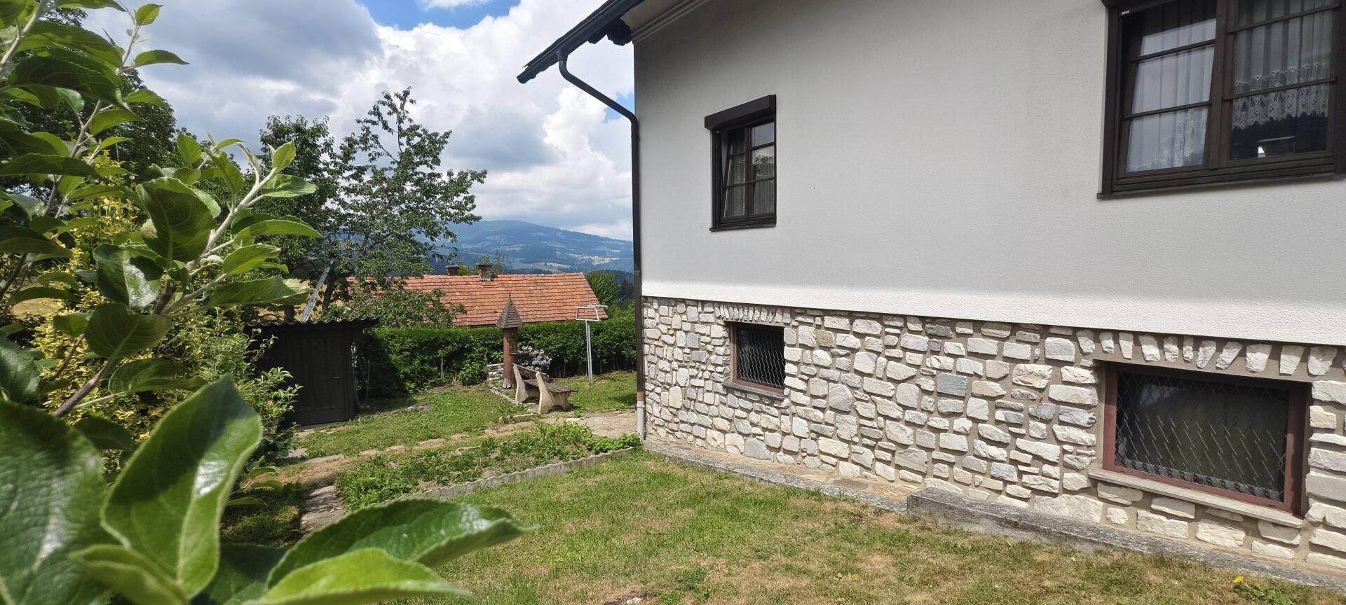 Seitenansicht des Hauses mit Steinsockel und Blick auf den Garten und die Landschaft.