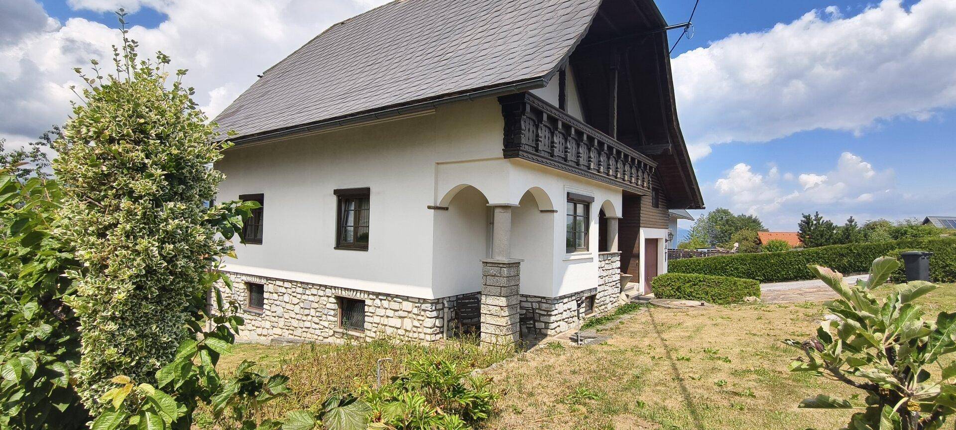 Traditionelles Haus mit Balkon, Steinsockel und gepflegtem Gartenbereich.