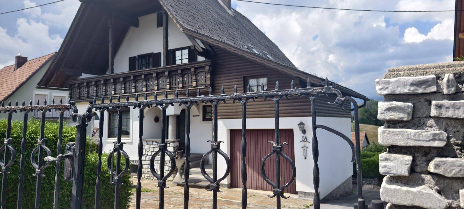 Traditionelles Haus mit schmiedeeisernem Tor, Balkon und Steinsockel.