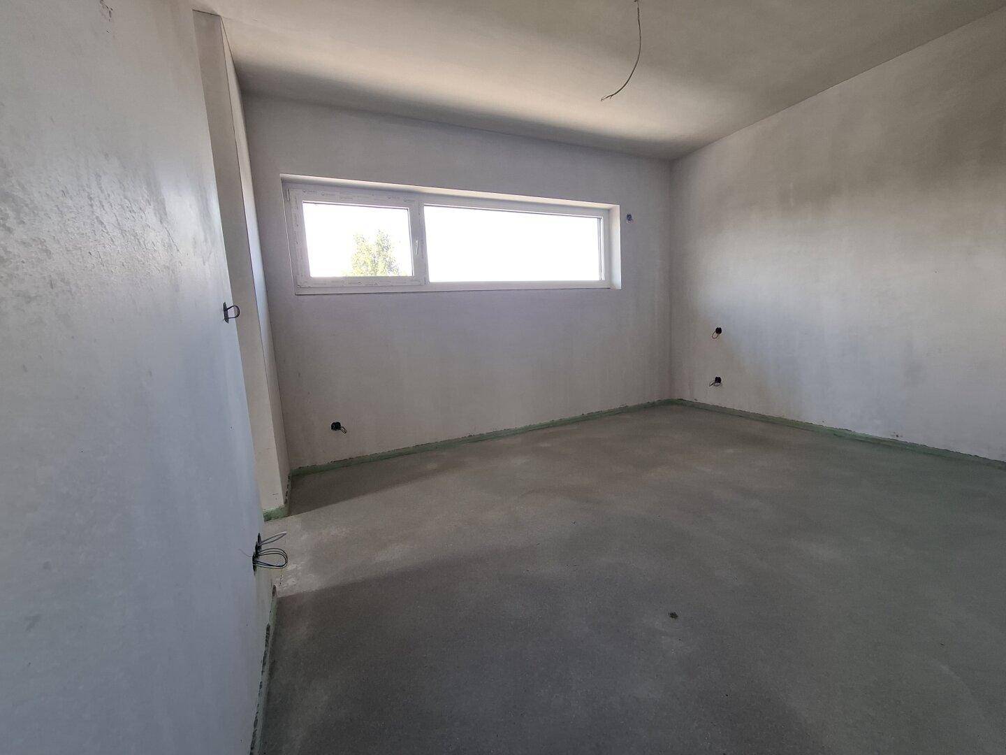 Unfertiges Schlafzimmer mit einem breiten Fenster, bereit für den Innenausbau.