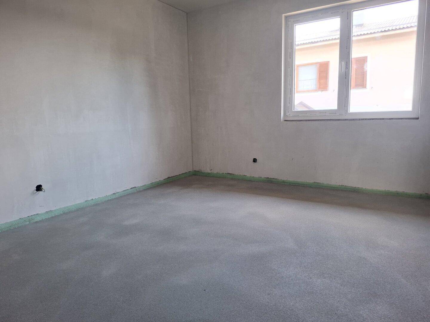 Unfertiges Zimmer mit Fenster und Blick auf die Nachbarbebauung, bereit für den Ausbau.