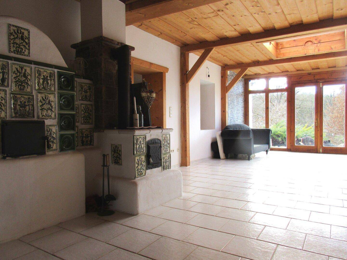 Helles Wohnzimmer mit traditionellem Kachelofen, Holzbalkendecke und Zugang zum Garten.