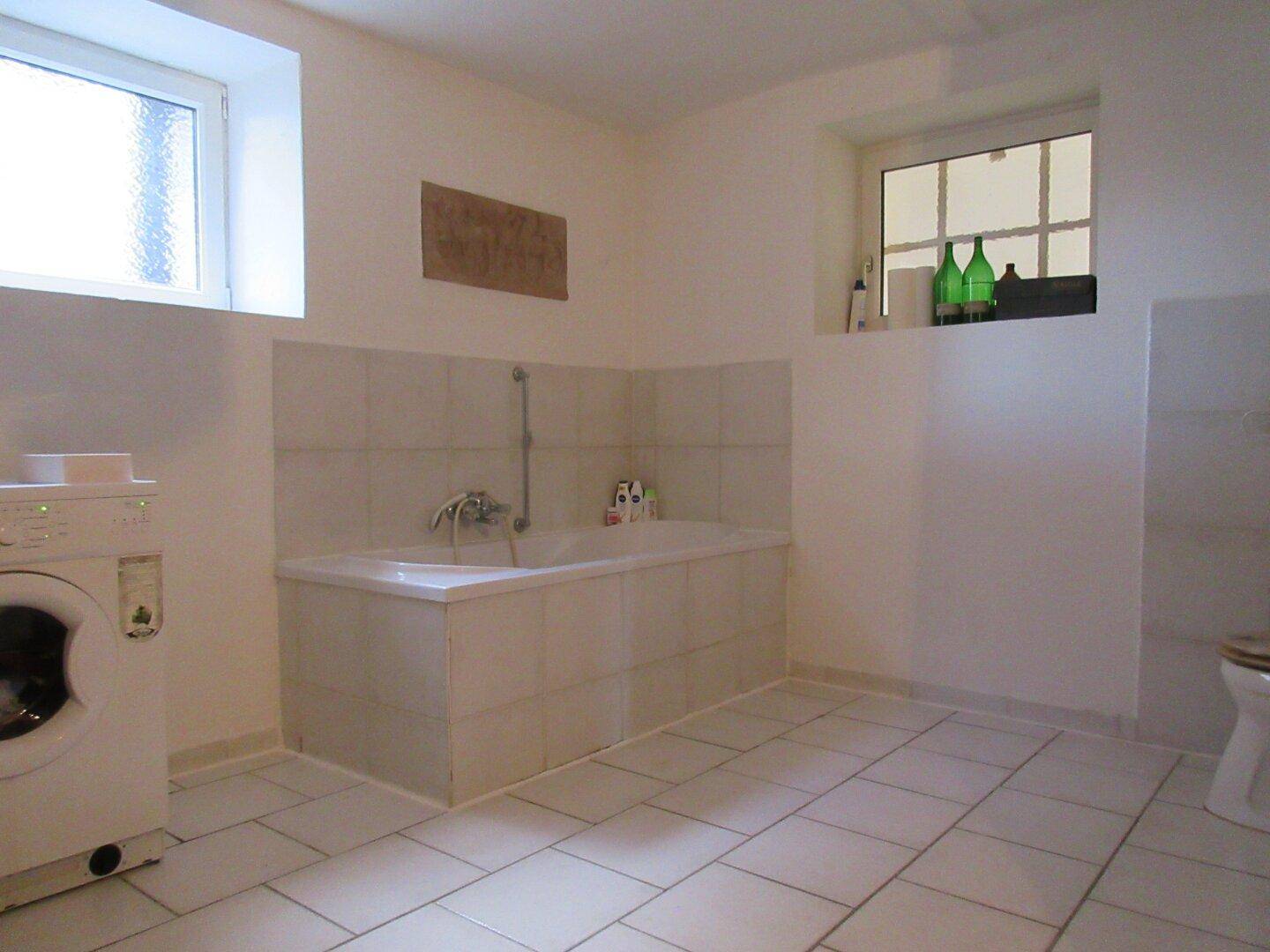 Geräumiges Badezimmer mit Badewanne, Waschmaschine und zwei Fenstern für Tageslicht.