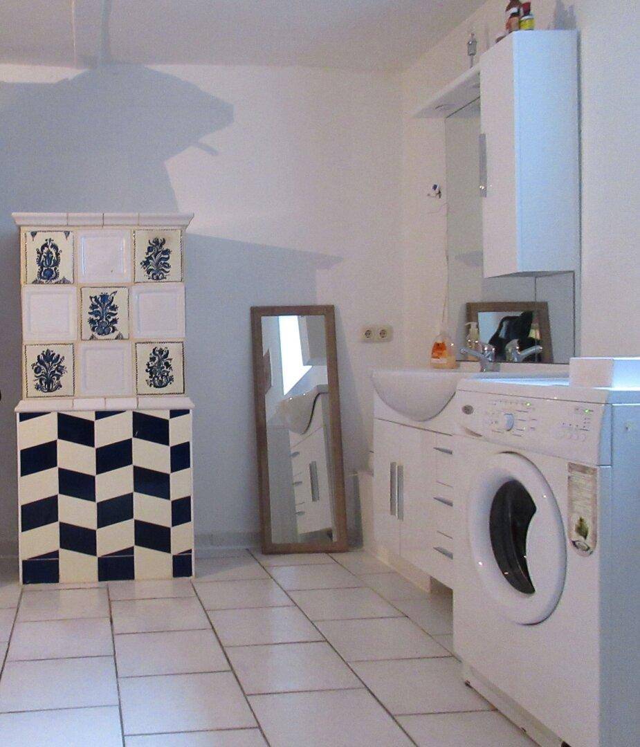 Funktionaler Waschraum mit Waschmaschine, Waschbecken und einem dekorativen Kachelofen.