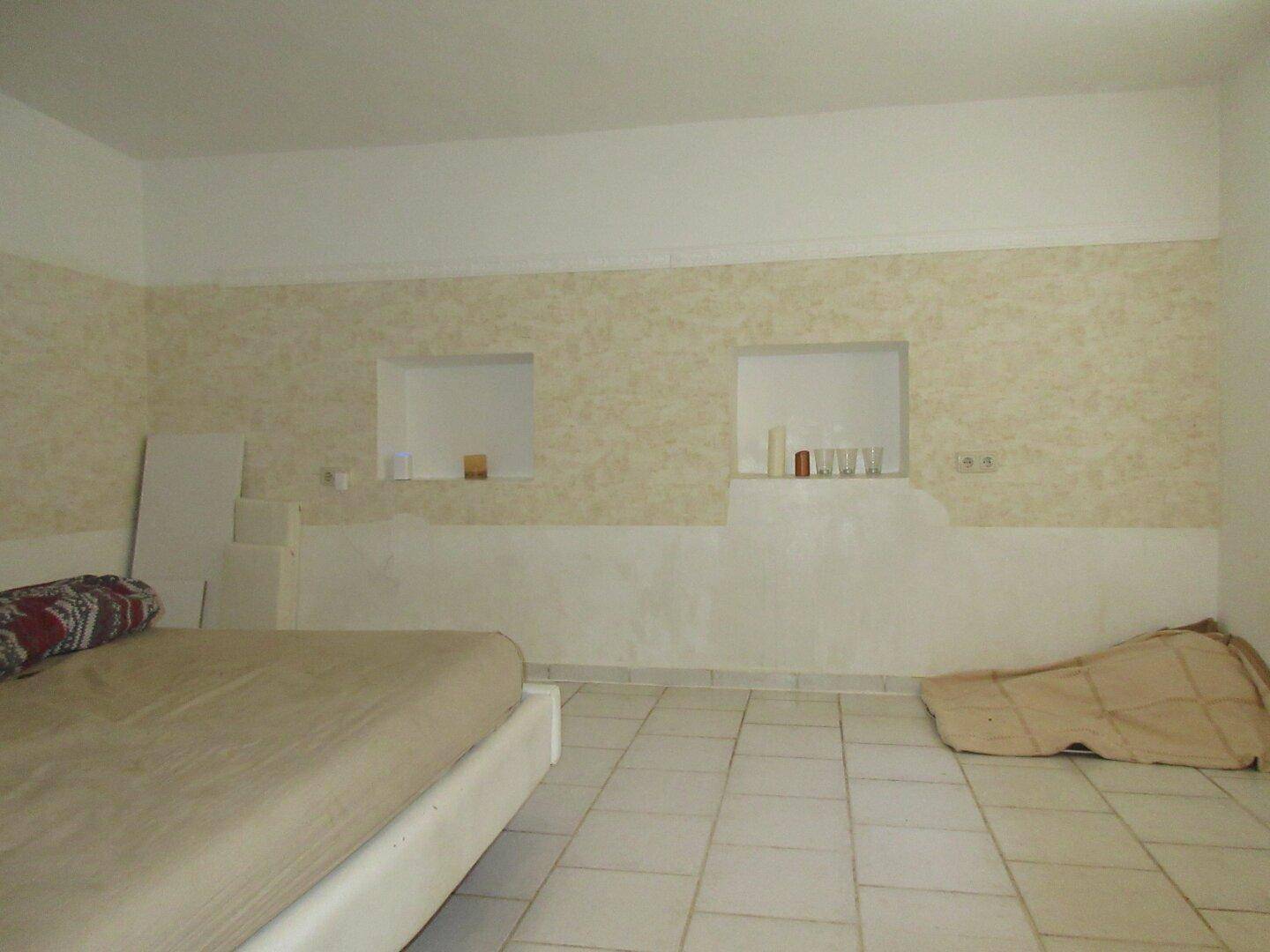 Schlafzimmer mit Fliesenboden, beiger Wandgestaltung und Nischen für Dekoration.