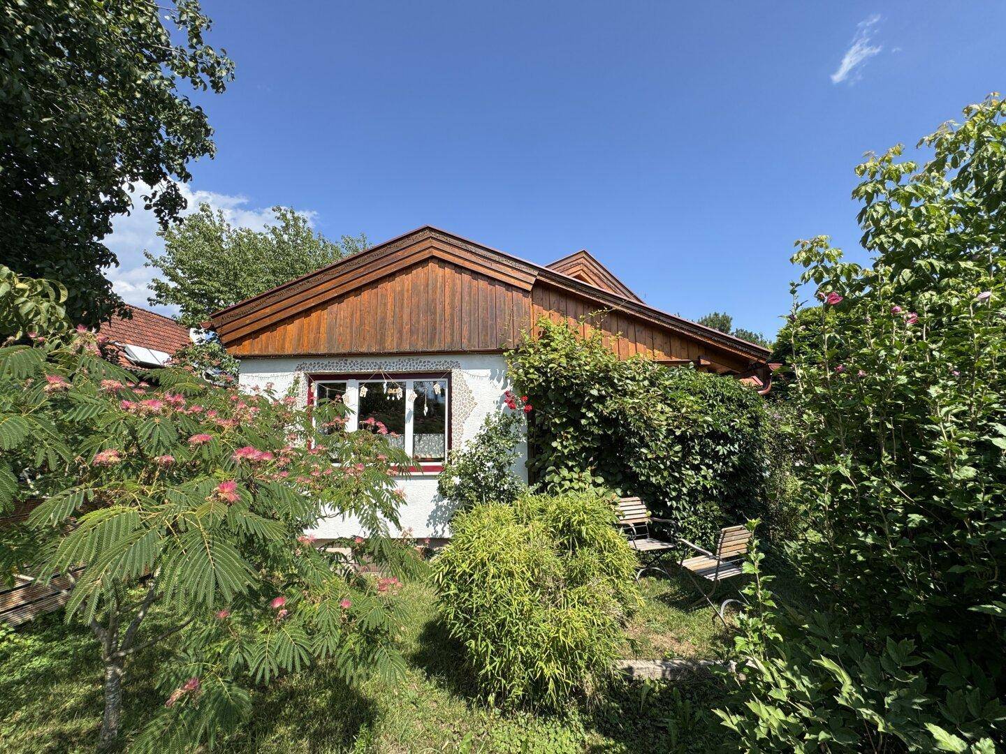 Rückseite eines Hauses mit weißer Fassade und Holzverkleidung, umgeben von üppigem Grün.