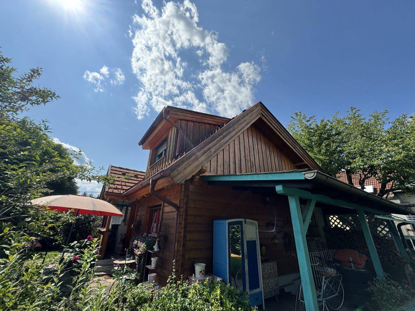 Rustikales Holzhaus mit überdachtem Eingangsbereich und rotem Dach unter strahlendem Himmel.