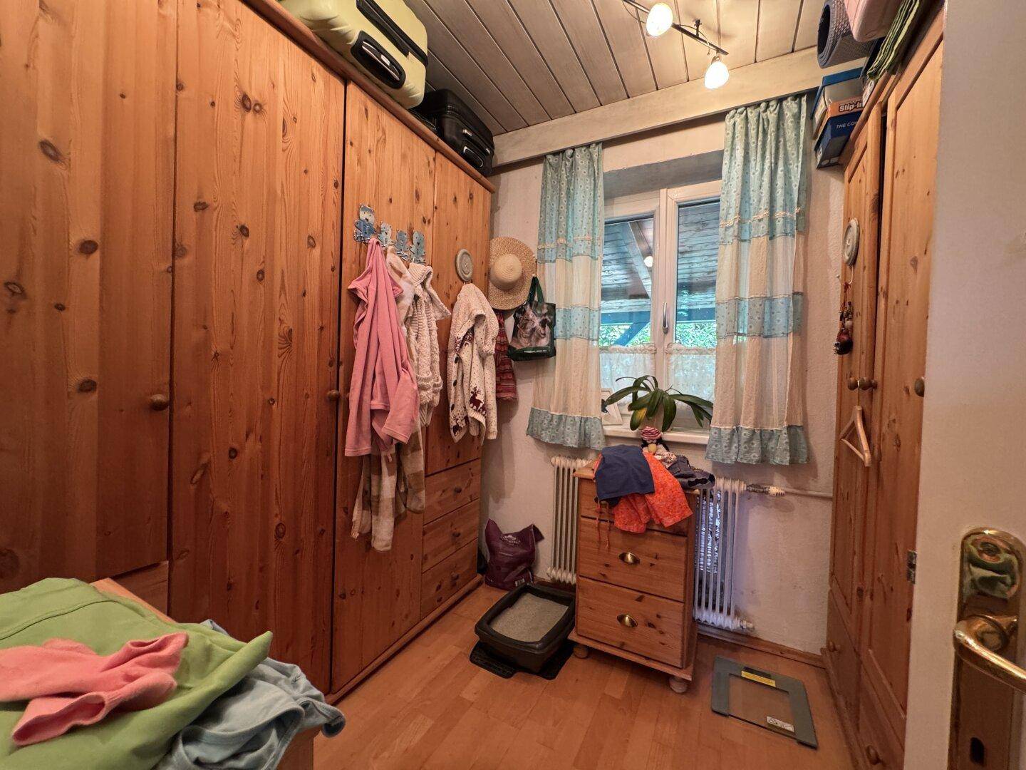 Schlafzimmer mit Holzschränken, Holzboden und Fenster mit Blick ins Grüne.