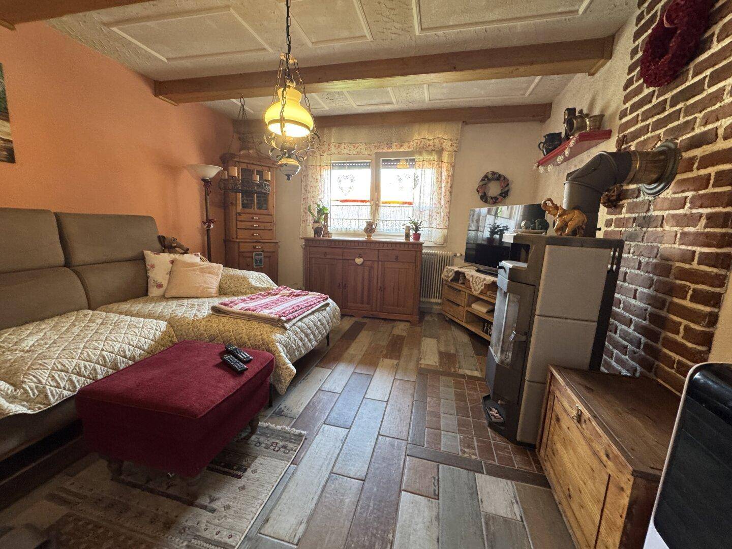 Gemütliches Wohnzimmer mit Kaminofen, Sofa und Holzbalkendecke.