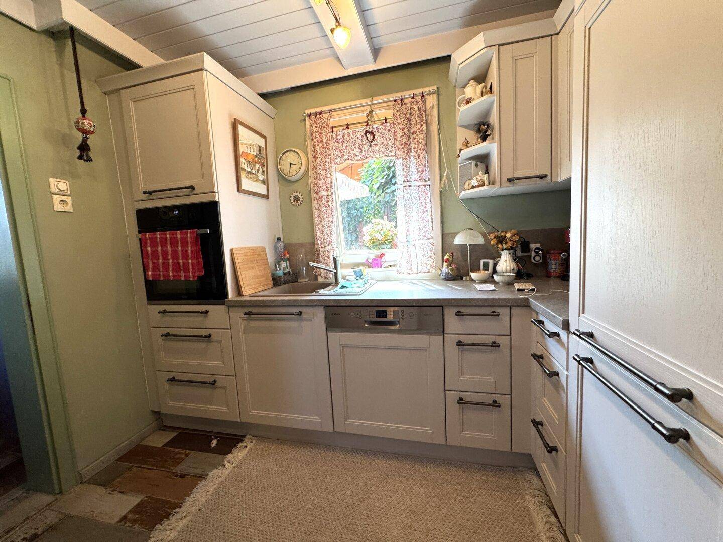 Funktionale Küche mit hellen Einbauschränken, Spülmaschine und Fenster mit Gartenblick.