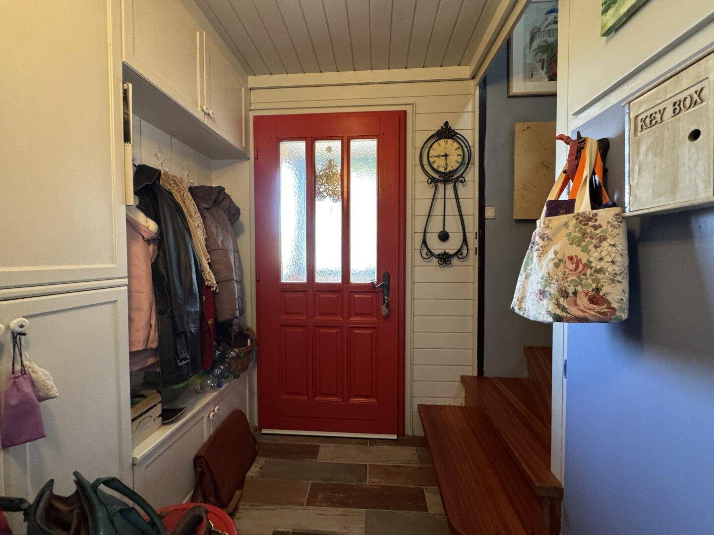 Gemütlicher Eingangsbereich mit roter Tür, Garderobe und Holztreppe zum Obergeschoss.