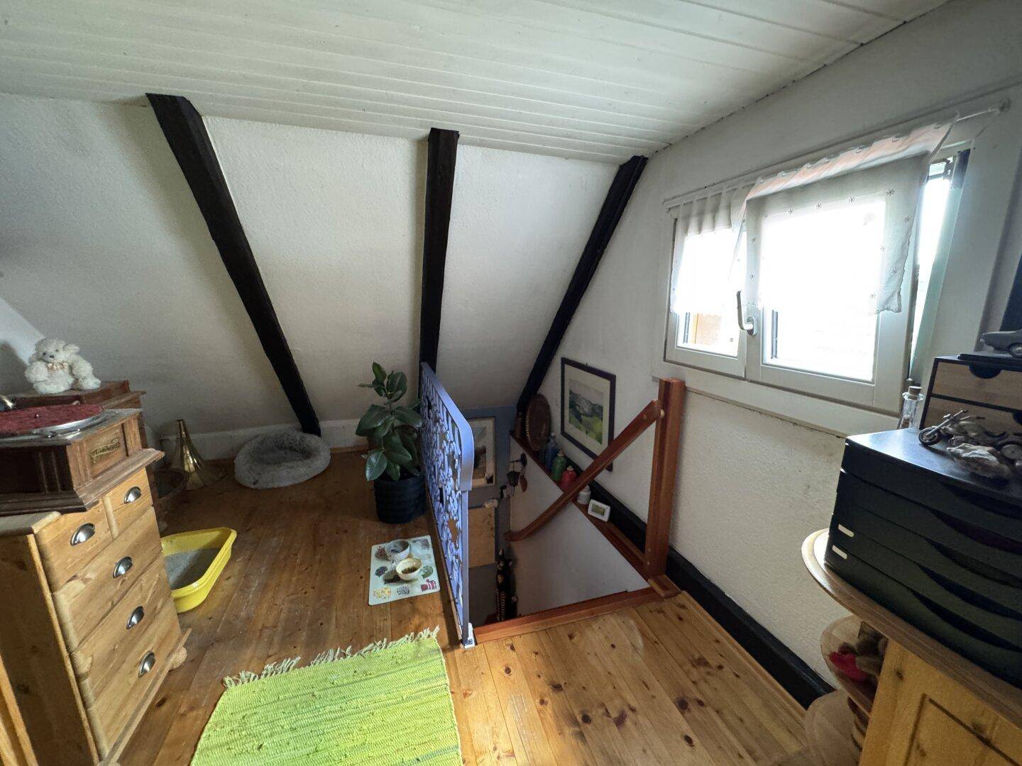 Dachgeschossbereich mit Holzfußboden, sichtbaren Holzbalken und Fenster.