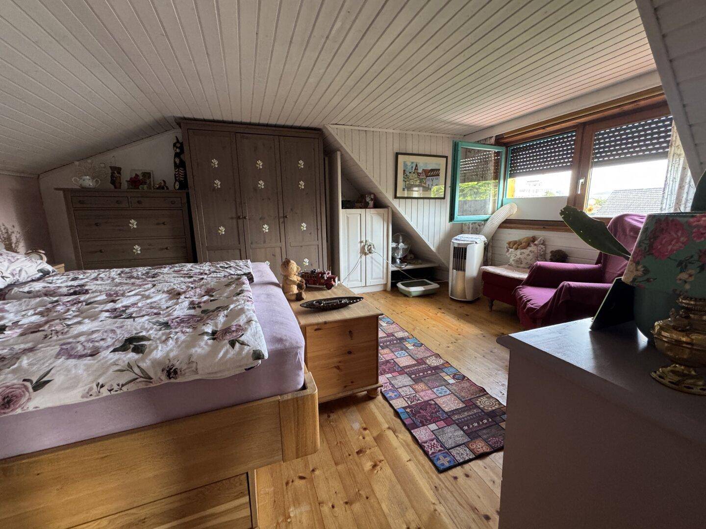 Schlafzimmer im Dachgeschoss mit Holzboden, Bett und Fenster mit Rollladen.