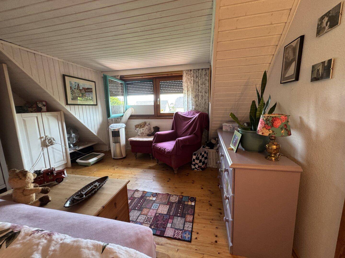 Helles Schlafzimmer im Dachgeschoss mit Holzboden, Sessel und Fenster.