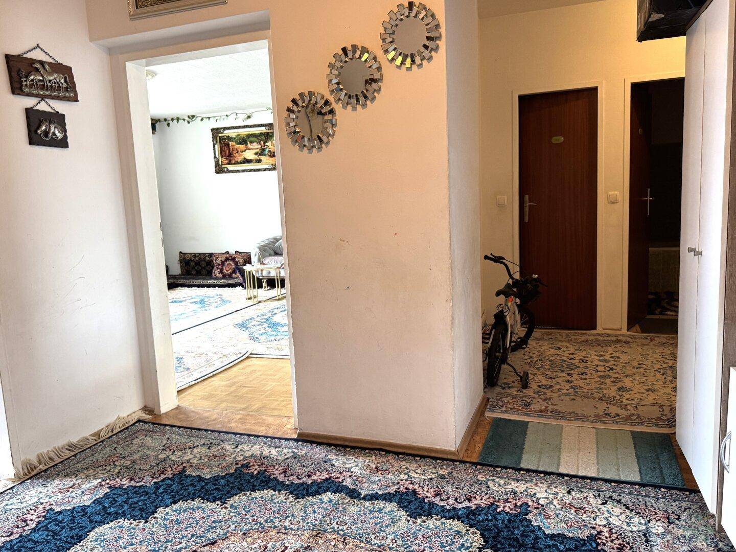 Heller Flur mit gemustertem Teppich, der zu den angrenzenden Wohnbereichen führt.