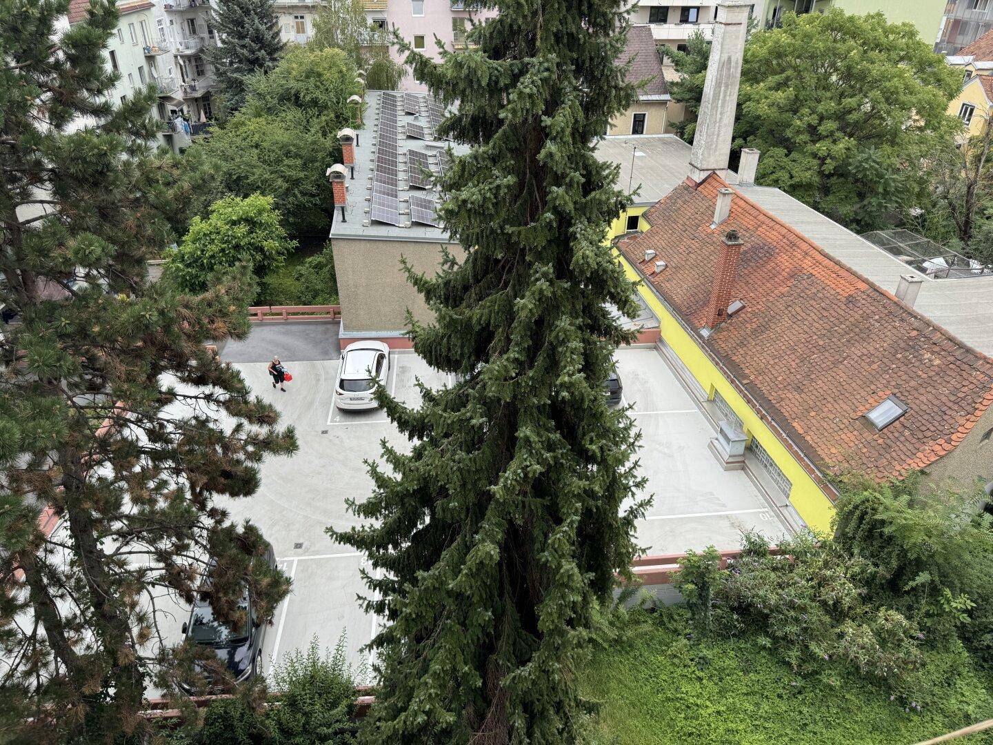 Luftaufnahme eines Parkplatzes mit Bäumen und Dächern, inklusive Solaranlagen auf einem Gebäude.