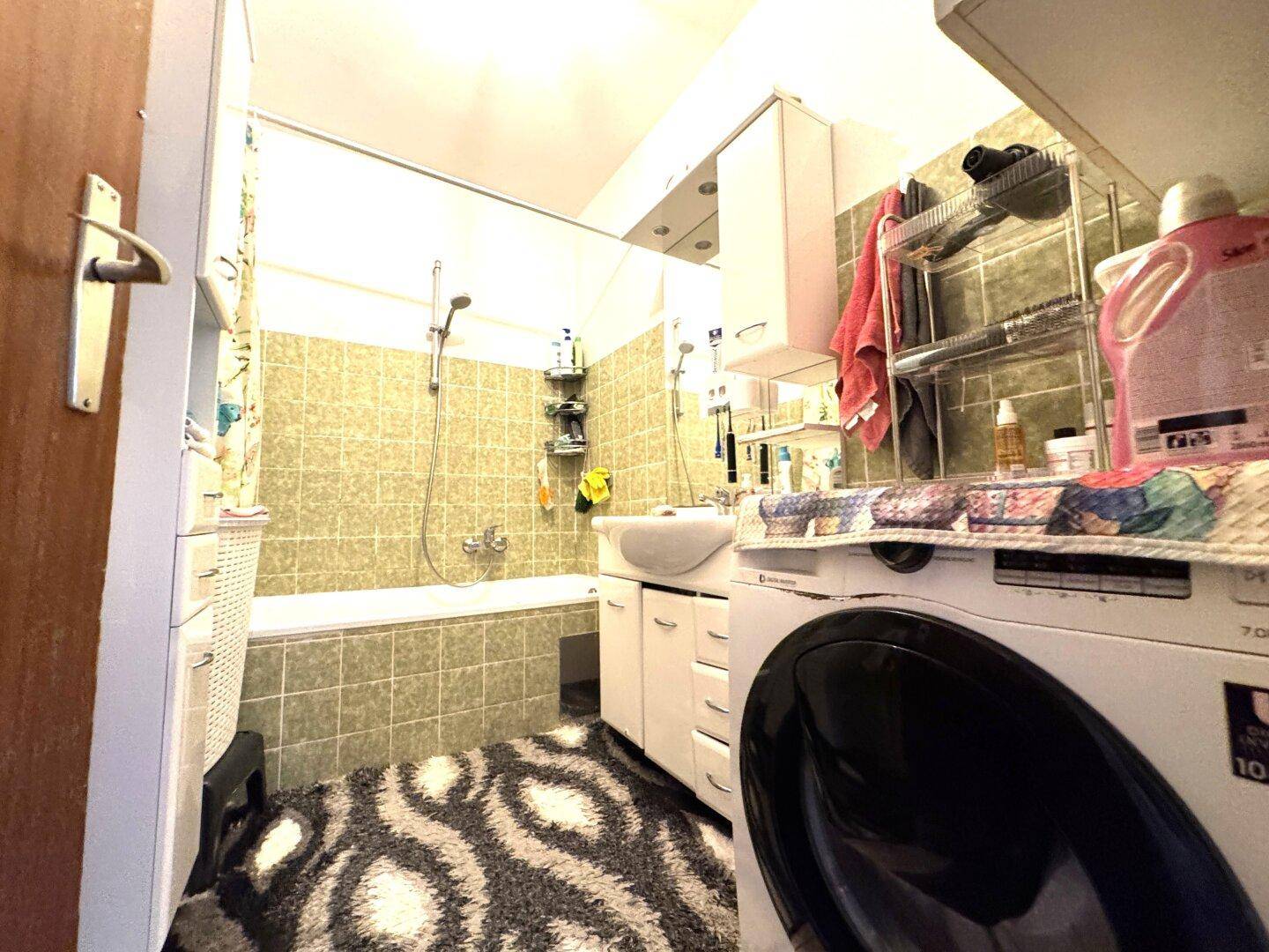 Badezimmer mit Badewanne, Duschfunktion, Waschbecken und einer Waschmaschine.