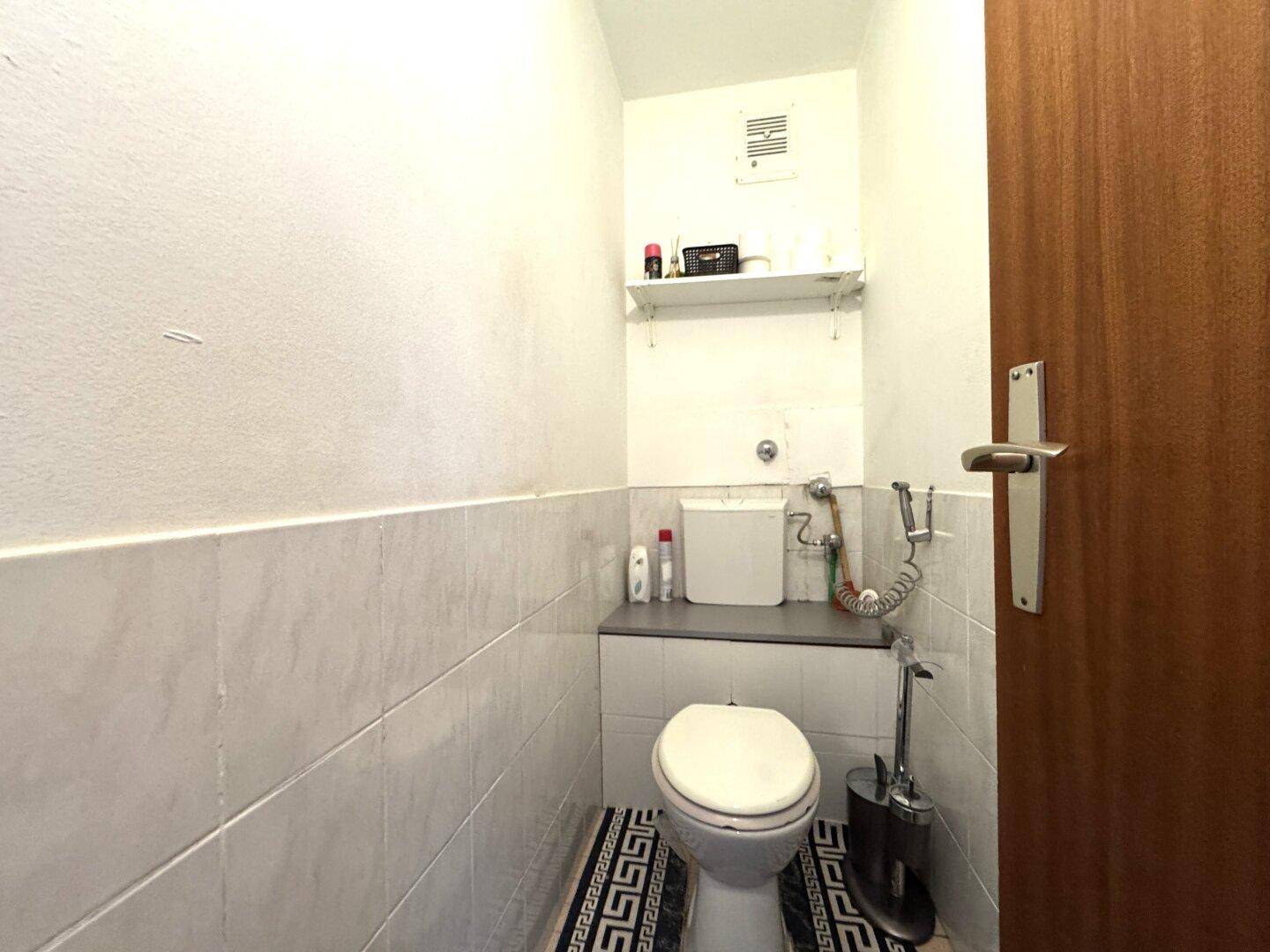 Separates WC mit Toilette, kleinem Waschbecken und weißen Wandfliesen.