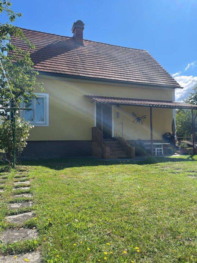 Gelbes Haus mit rotem Ziegeldach und gepflegtem Rasen, der zum Eingang führt.