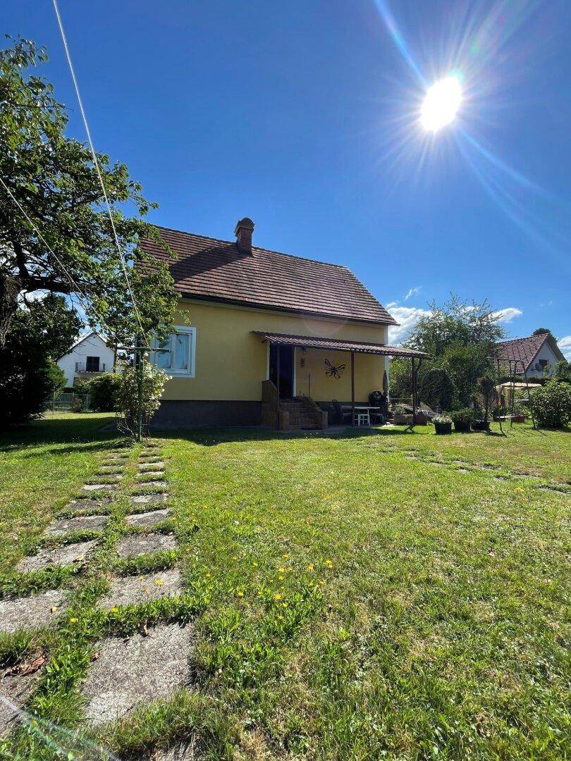 Freistehendes gelbes Haus mit rotem Ziegeldach und weitläufigem Rasen unter strahlendem Himmel.